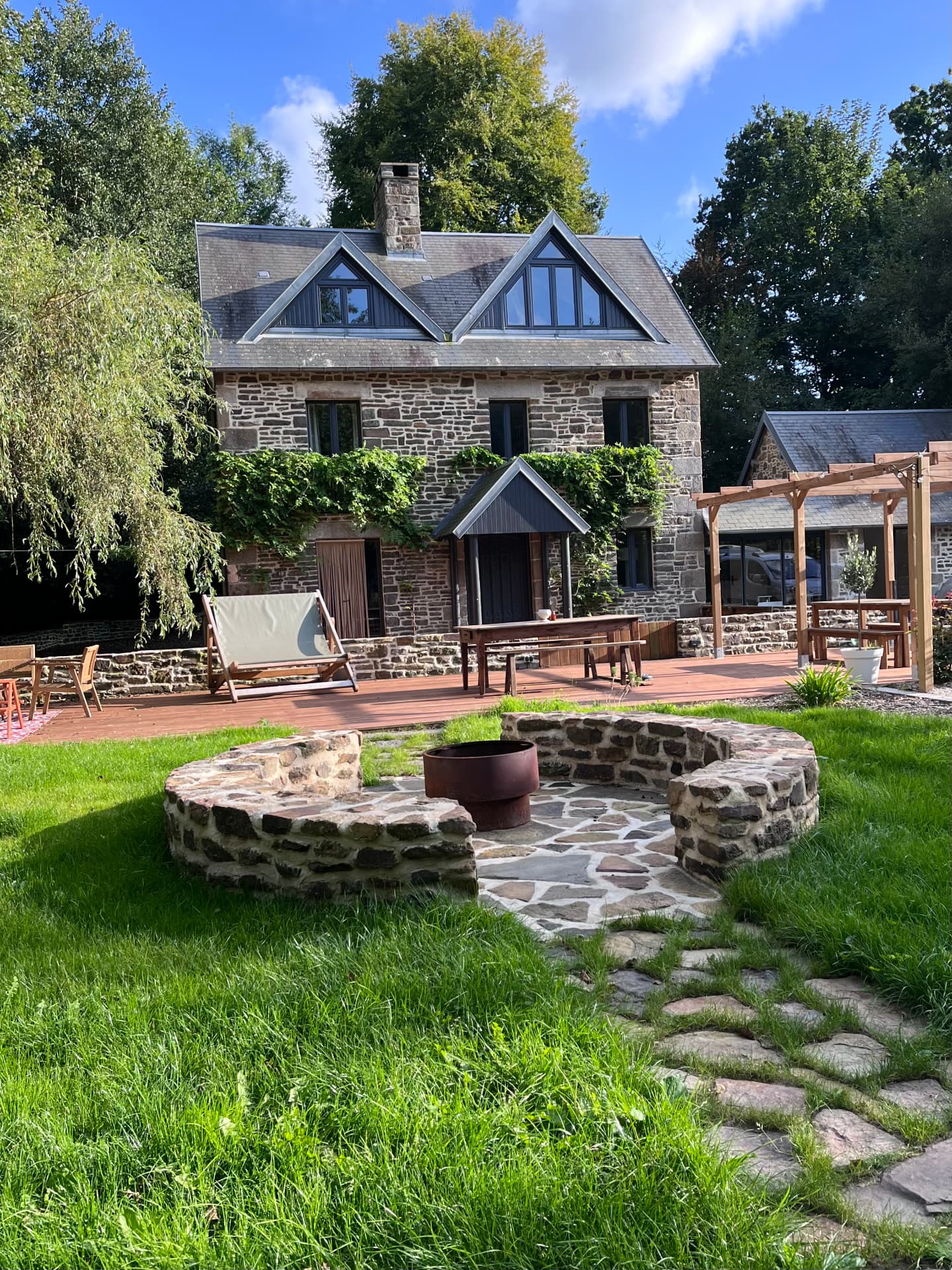 The Sanctuary — the stone mill house, its deck and the fire pit on the sunlit lawn